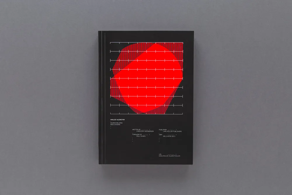 A book with a black cover featuring a large, abstract red shape on the center. The shape is overlaid with white grid lines. Some small white text is present below the red shape, but it is not readable in detail. The background is gray.