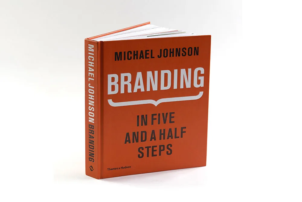 A book titled "Branding: In Five and a Half Steps" by Michael Johnson, published by Thames & Hudson. The cover is orange with white and black text.