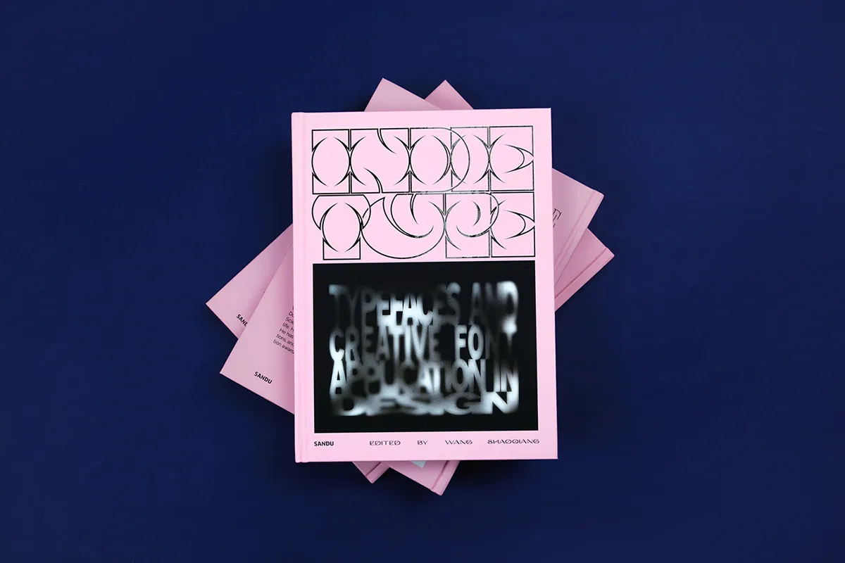 A pink book with a geometric pattern on the top half of the cover and a blurred, abstract text design on the bottom half. The book is stacked on top of two identical copies against a dark blue background. .